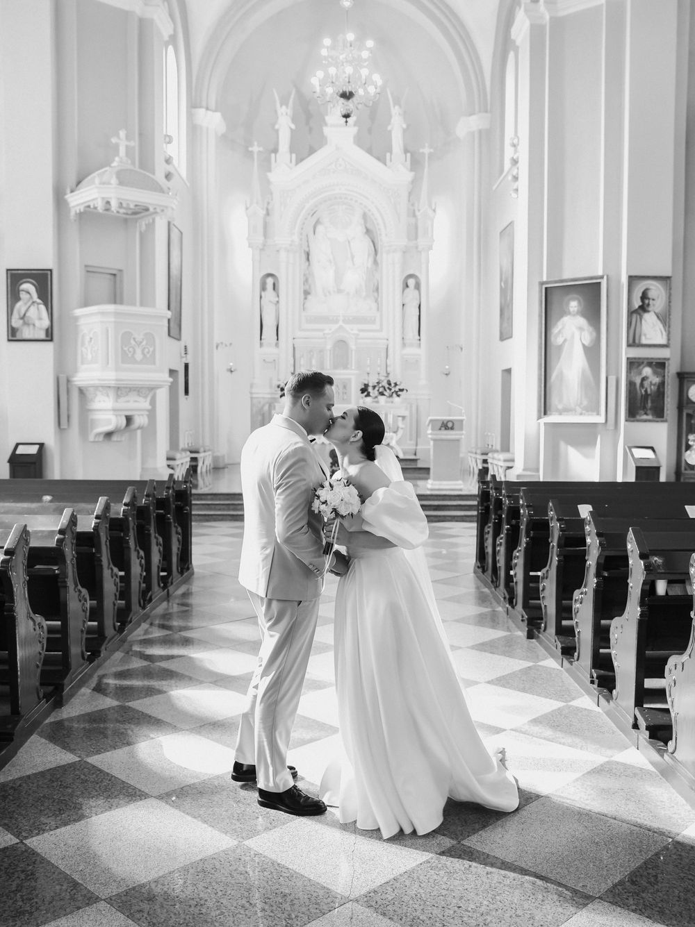 Black and white wedding photos show a couple dancing in the sunlit aisle of a grand cathedral with ornate architecture.