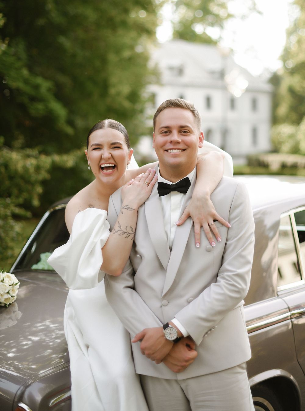 Candid wedding photos showing joyful moments between a couple in white formal attire next to a vintage car.