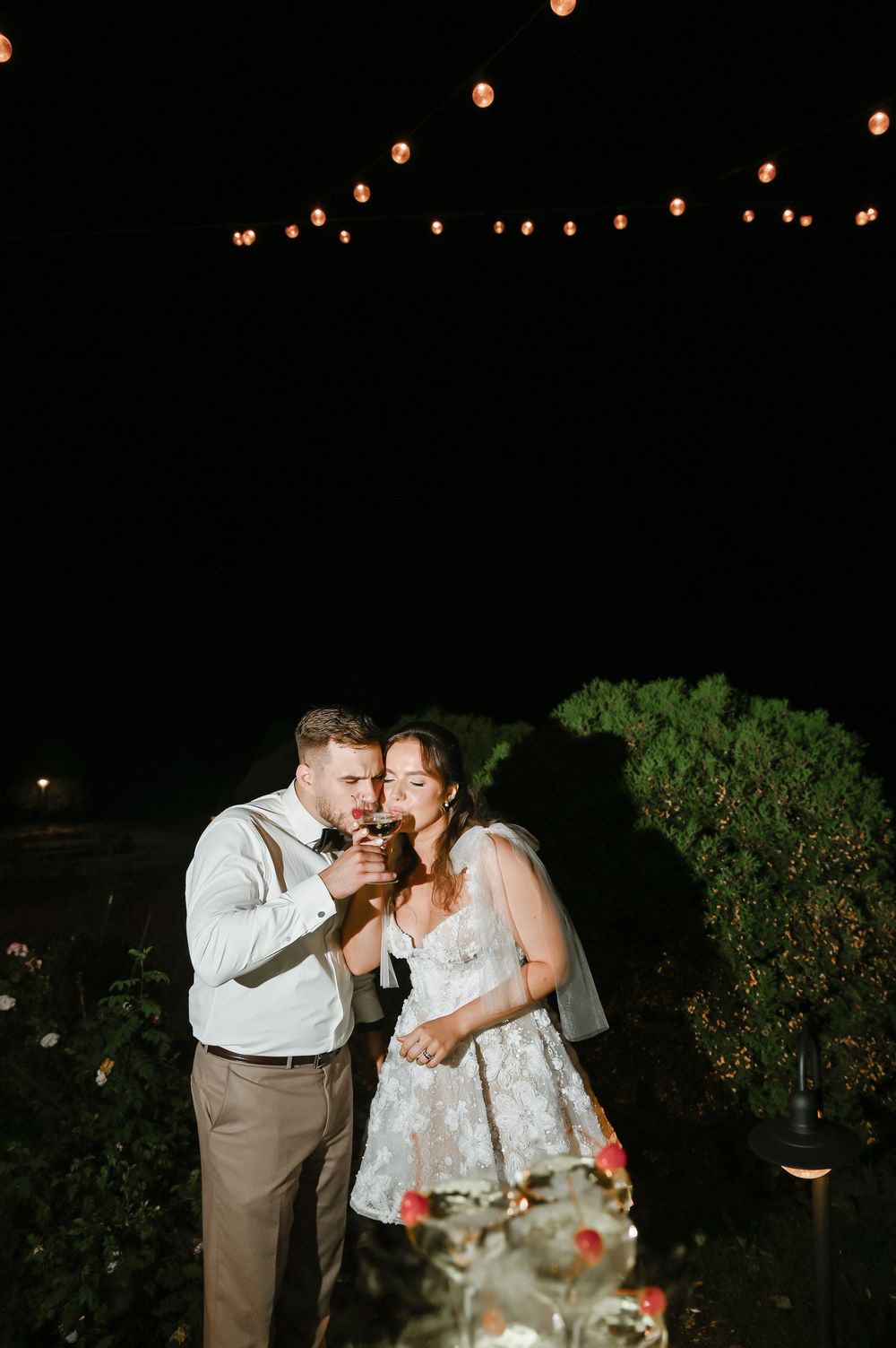 A couple shares a romantic moment under glowing lantern lights in an outdoor evening garden setting.