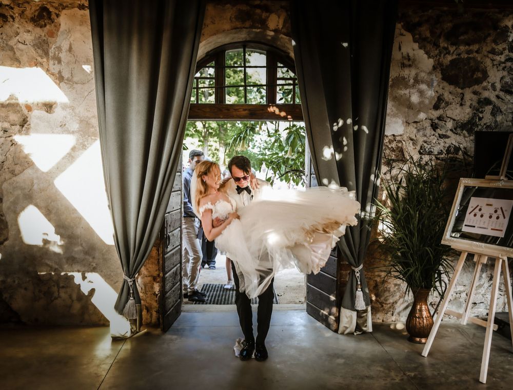 Playful wedding moment captured in rustic venue with dramatic lighting and drapes.
