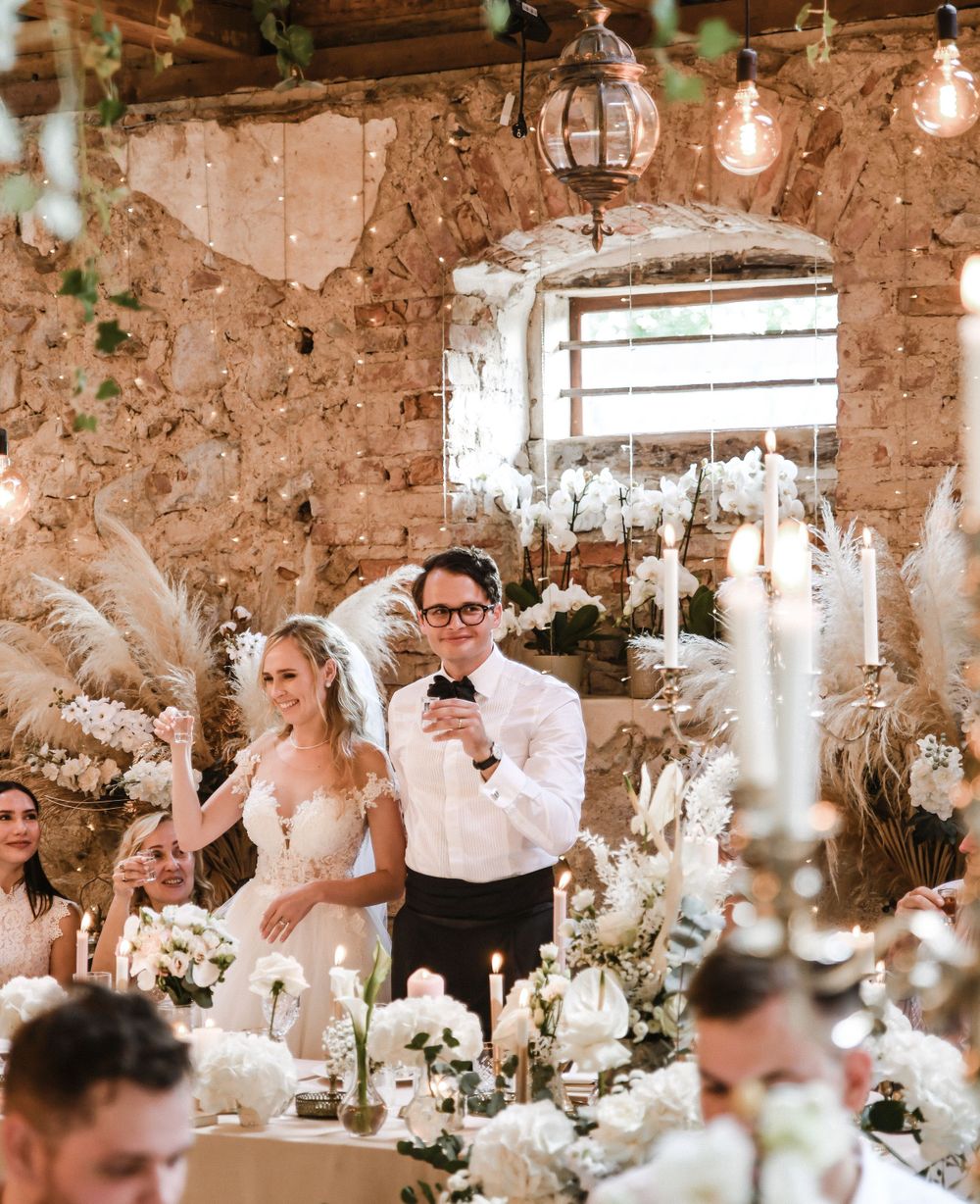Rustic stone reception hall decorated with hanging lights and white floral arrangements for an elegant wedding celebration.