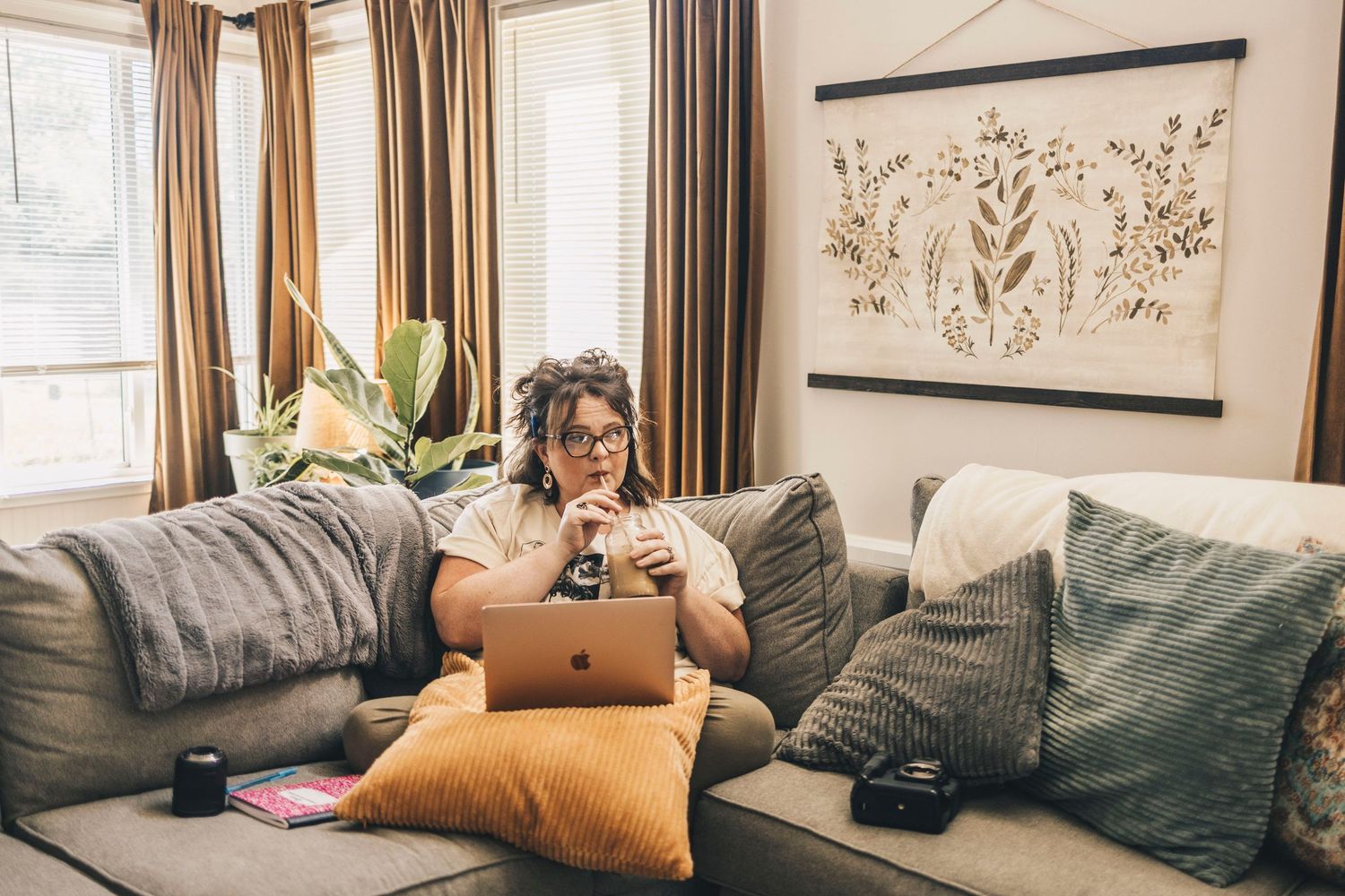 Woman with curly hair working on laptop while sitting on cozy couch at home.