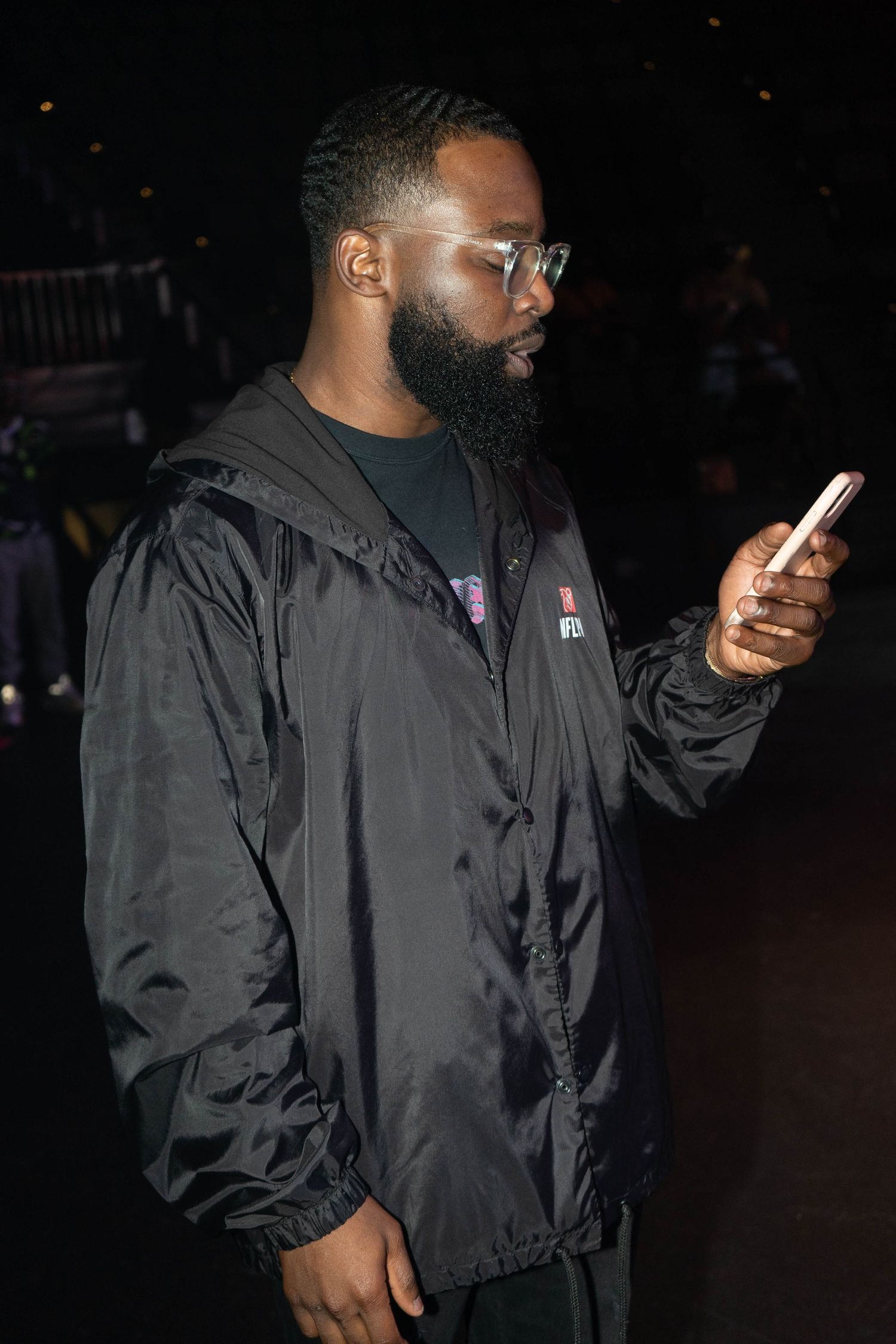 A person in a black jacket checks their phone while standing in a dimly lit space.