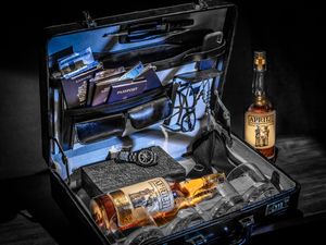 A collection of gun cases and whiskey bottles illuminated by dramatic lighting showcases premium firearms and bourbon.