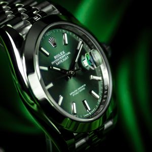 Luxury Rolex watch with green dial and metal bracelet photographed in dramatic emerald lighting.