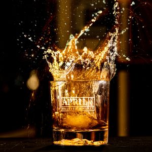Golden liquid splashing in a whiskey glass with dramatic dark background. April One Bourbon Shoot