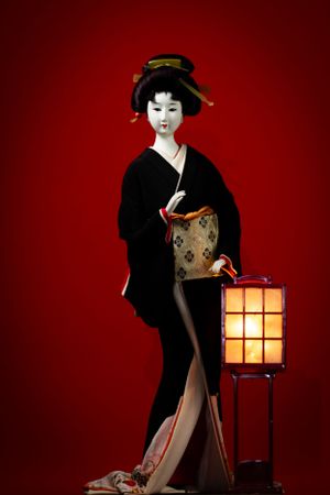 Geisha figurine in black kimono standing beside illuminated paper lantern. Luxury product photography.