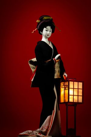 Traditional Japanese geisha doll with lantern against deep red background. Luxury product photography.