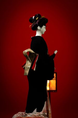 A traditional Japanese geisha in black kimono poses elegantly against a deep red background. Luxury product photography.