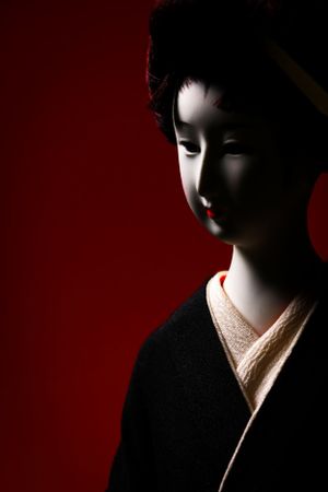Dramatic side profile of geisha doll head against dark red background. Luxury product photography.