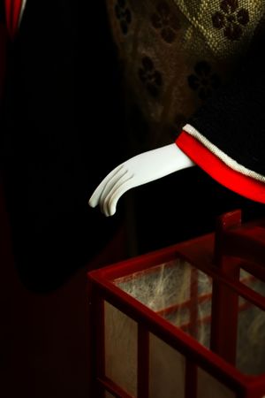 Close-up detail of white gloved hand near red paper lantern. Luxury product photography.