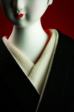 Close-up of geisha doll showing white face makeup and traditional collar. Luxury product photography.