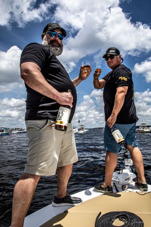 Two people enjoying drinks on a boat deck with boats and water in background. Editorial product photography. April One Bourbon Shoot