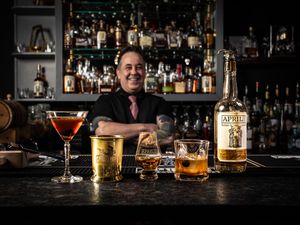 A well-stocked bar counter displays various cocktails and spirits, including a martini glass and whiskey bottles in warm lighting.