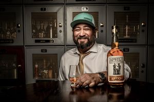 Person holding a bottle of Old Forester bourbon whiskey while smiling in a dimly lit bar setting.