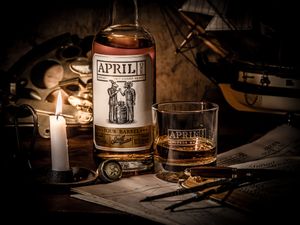 A bottle of April vodka and glass with candlelight and vintage tools create a moody, atmospheric still life.