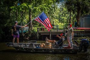 American flags wave proudly at a serene lakeside dock surrounded by lush greenery on a summer day.