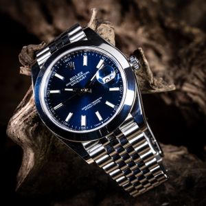 A luxury silver and blue dial watch displayed on driftwood in dramatic lighting.