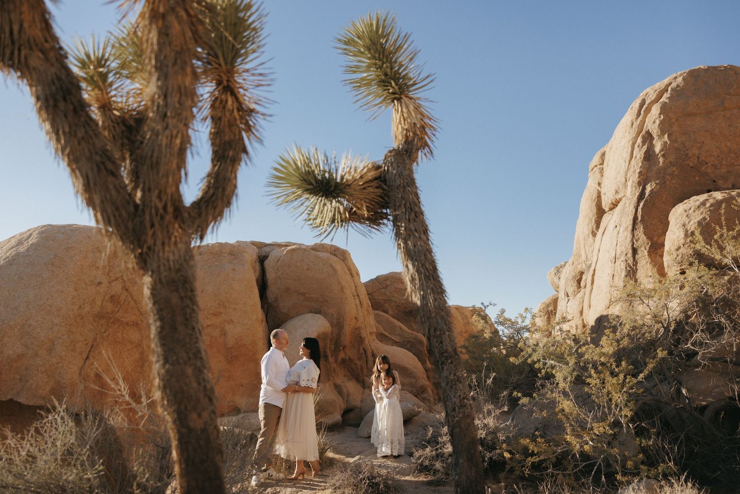 Couple in white attire exchange vows among Joshua trees and boulders in Joshua Tree National Park.