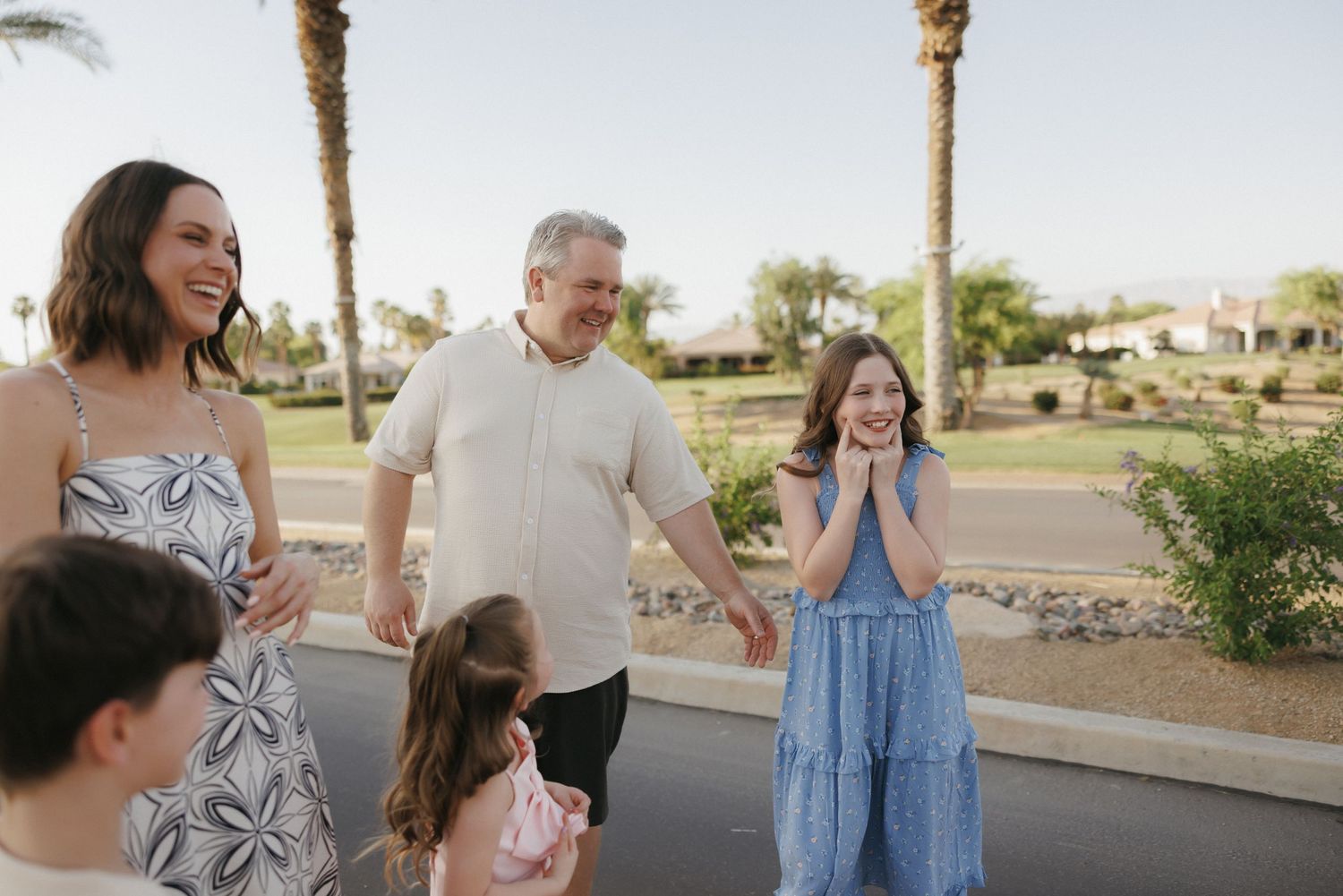 Happy family walking together outdoors near palm trees on a sunny day in a residential neighborhood.