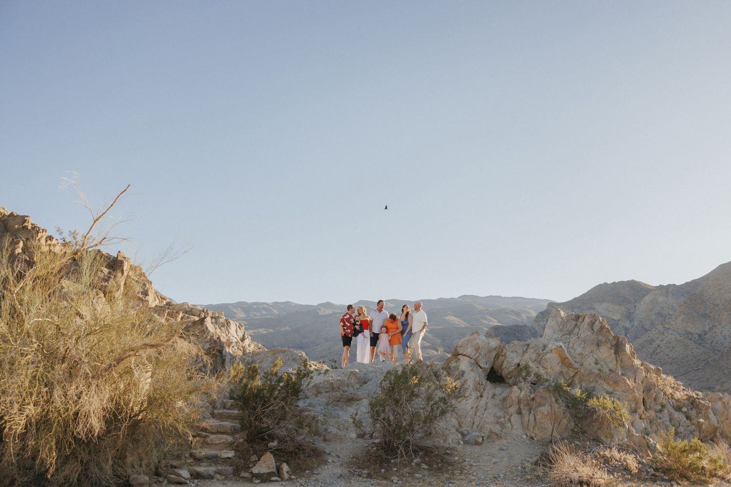 Group of people standing on rocky desert terrain with mountains and clear sky in the background.