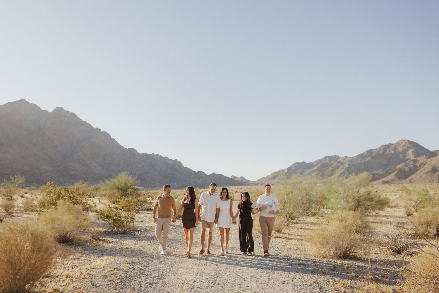 Group of five people walking on a desert path with mountains and clear blue sky in the background.