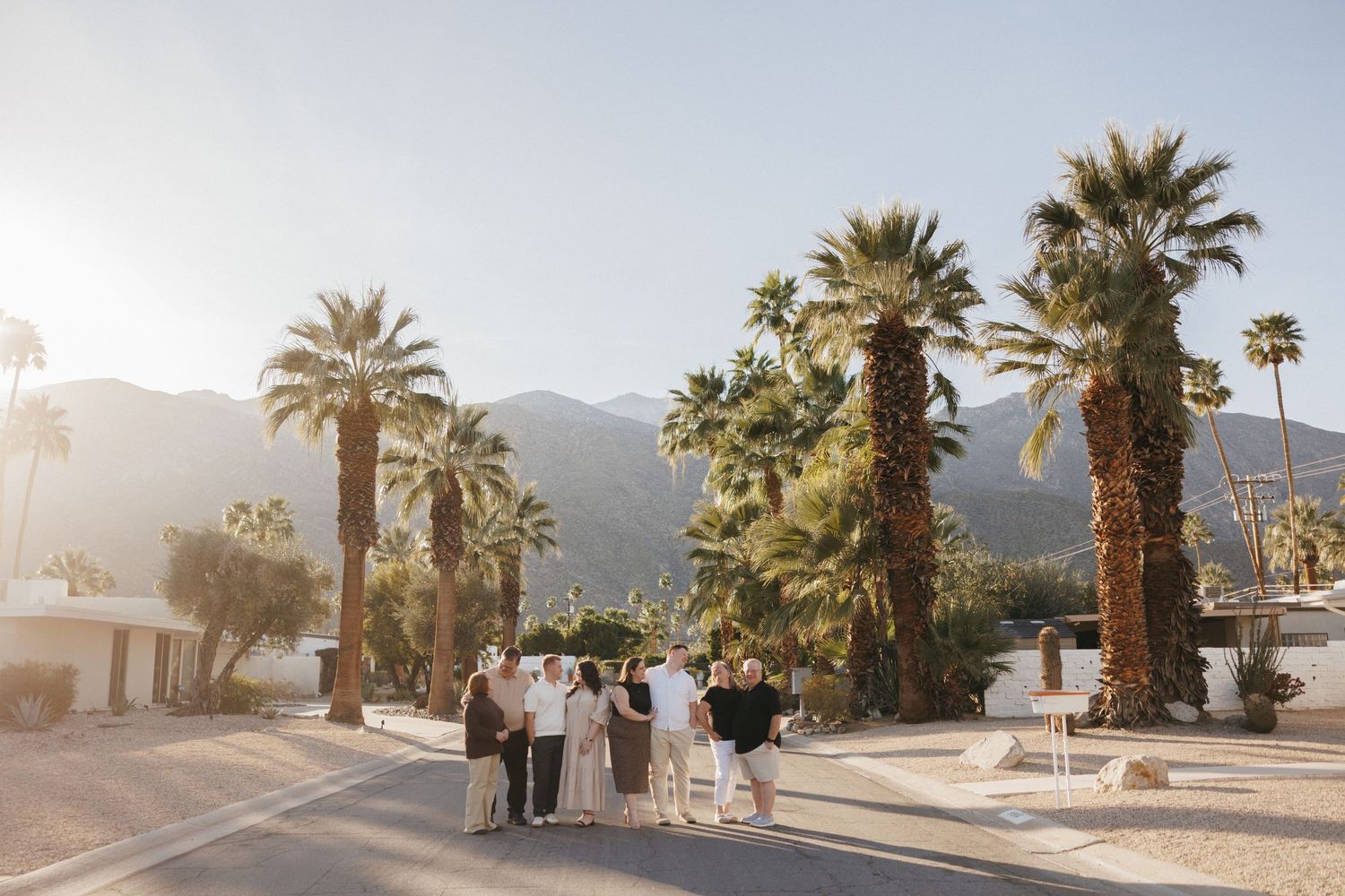 Small wedding ceremony group stands on a sunny Palm Springs street lined with tall palm trees and mountain backdrop.