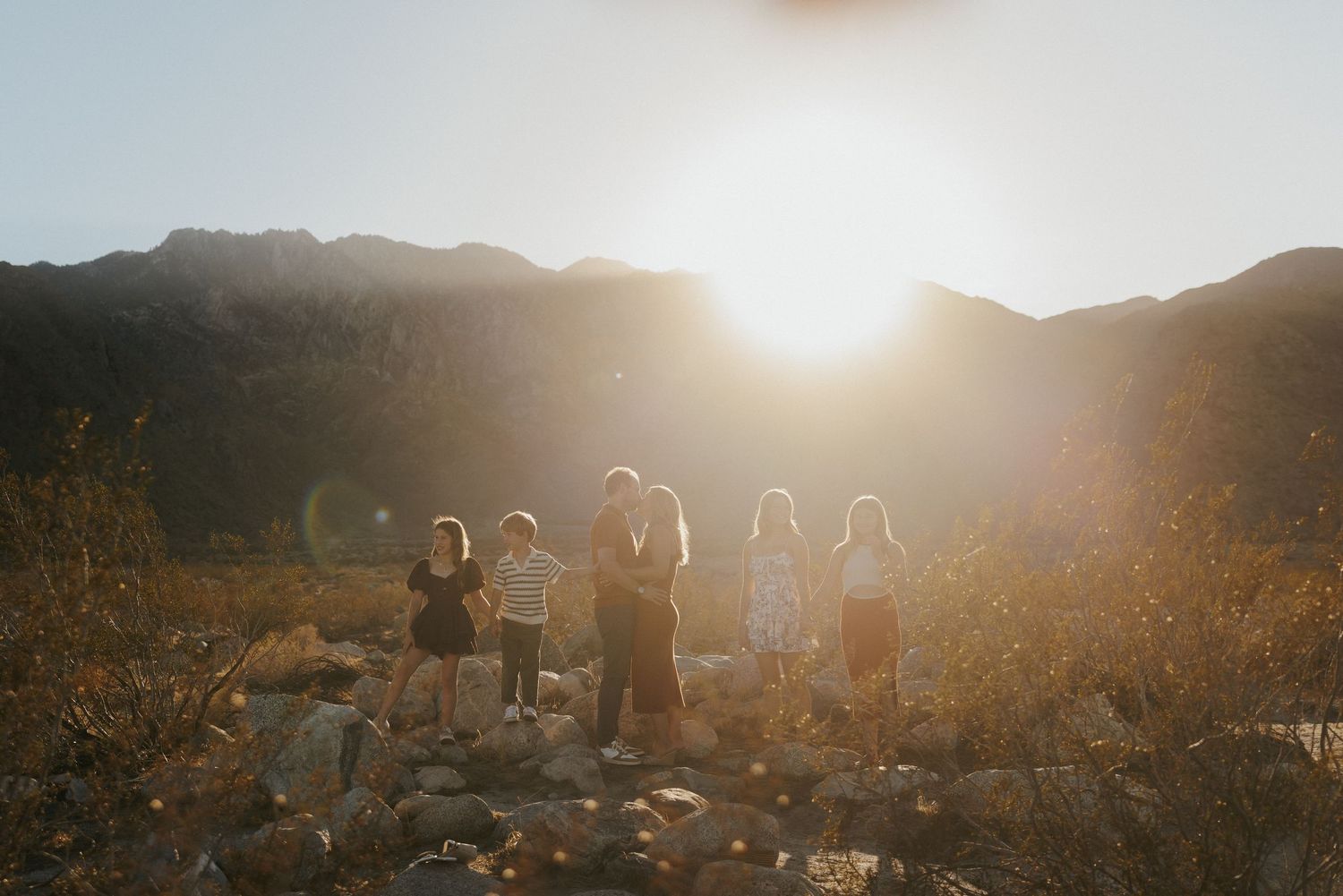 Group of children and adults silhouetted against golden sunset in rocky mountain landscape.