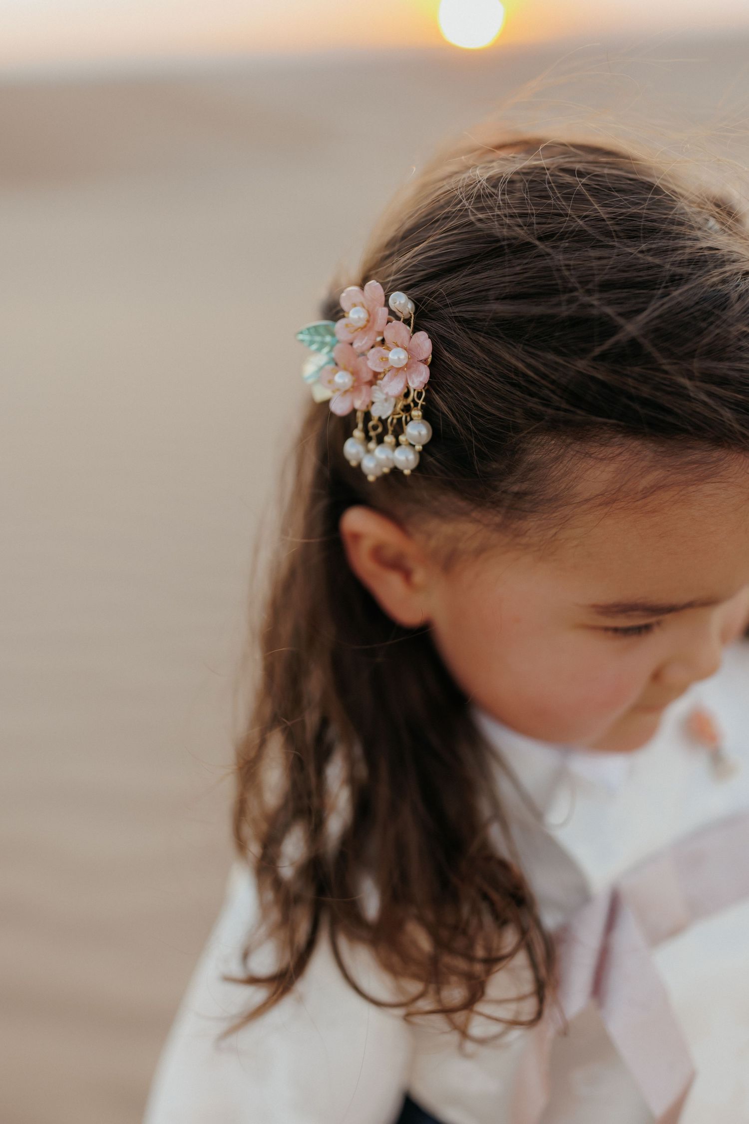 Young girl with dark hair wearing a delicate pink floral hair clip with pearls, photographed at sunset.