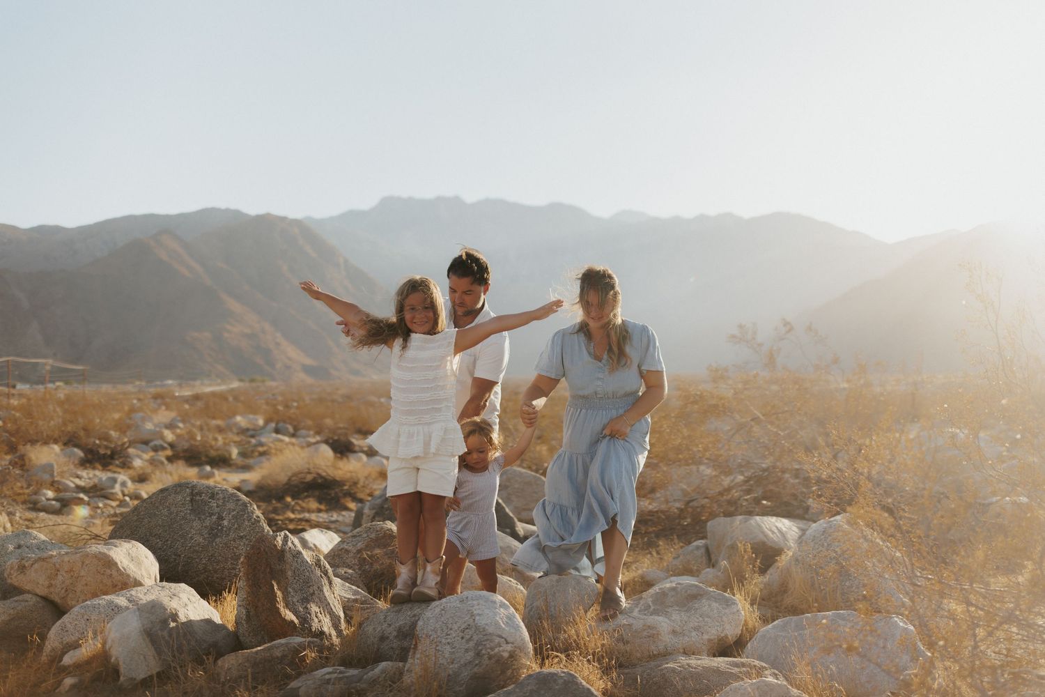 Family of four posing on rocks in a sunny desert landscape with mountains in the background.