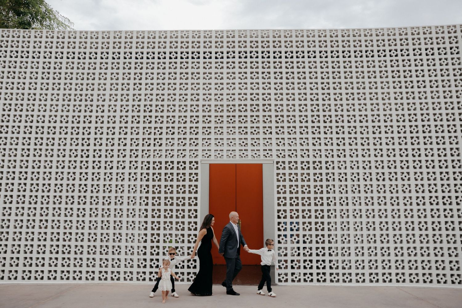 People standing by a red door set in a decorative white geometric patterned wall at an outdoor venue.