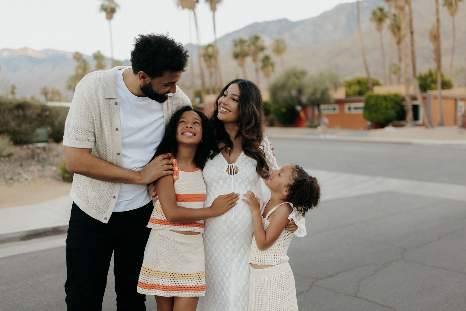 Happy family of four smiling outdoors in Palm Springs with mountains and palm trees in the background.