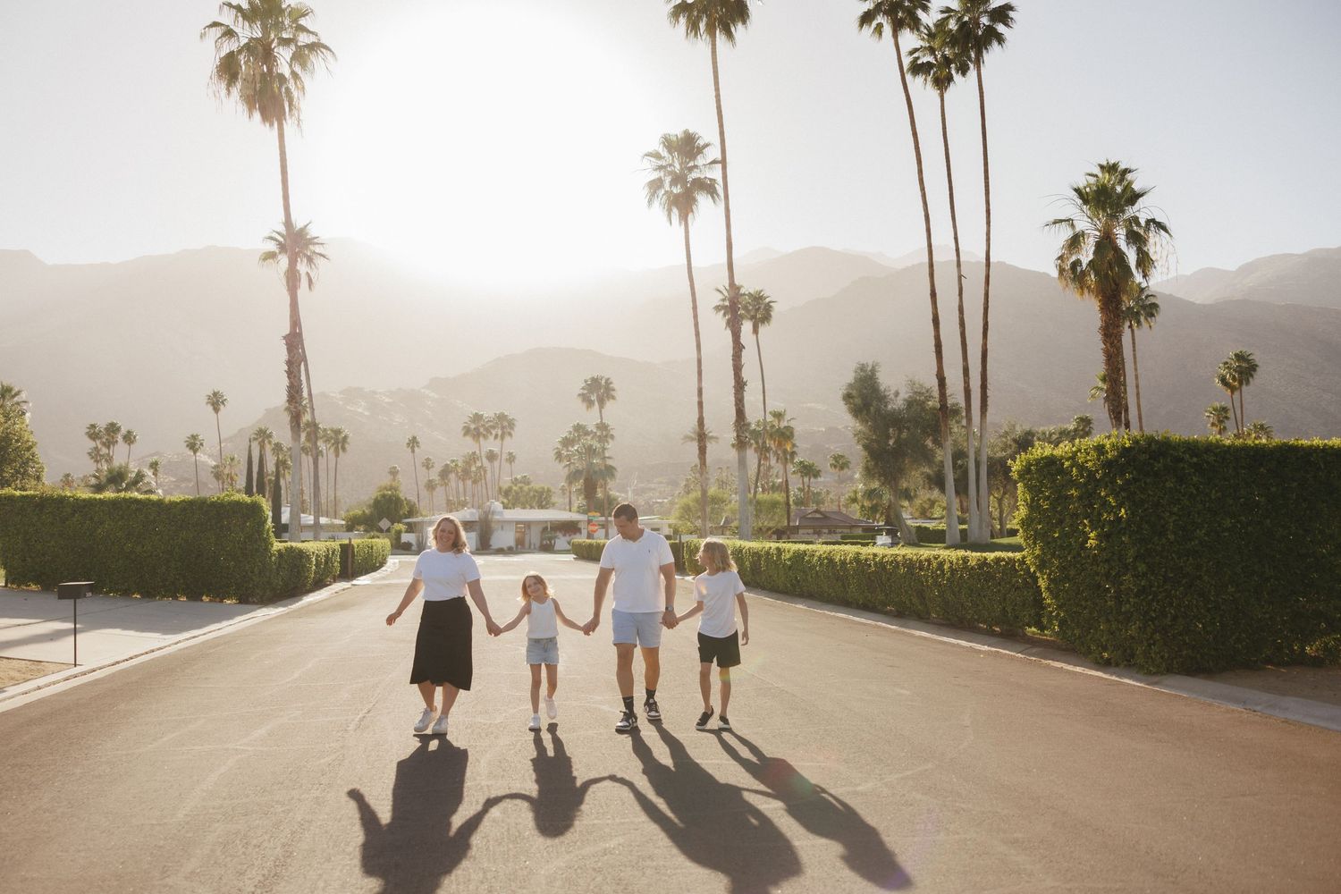 Family holding hands on a sunny palm-lined street with mountains in the background in Palm Springs.