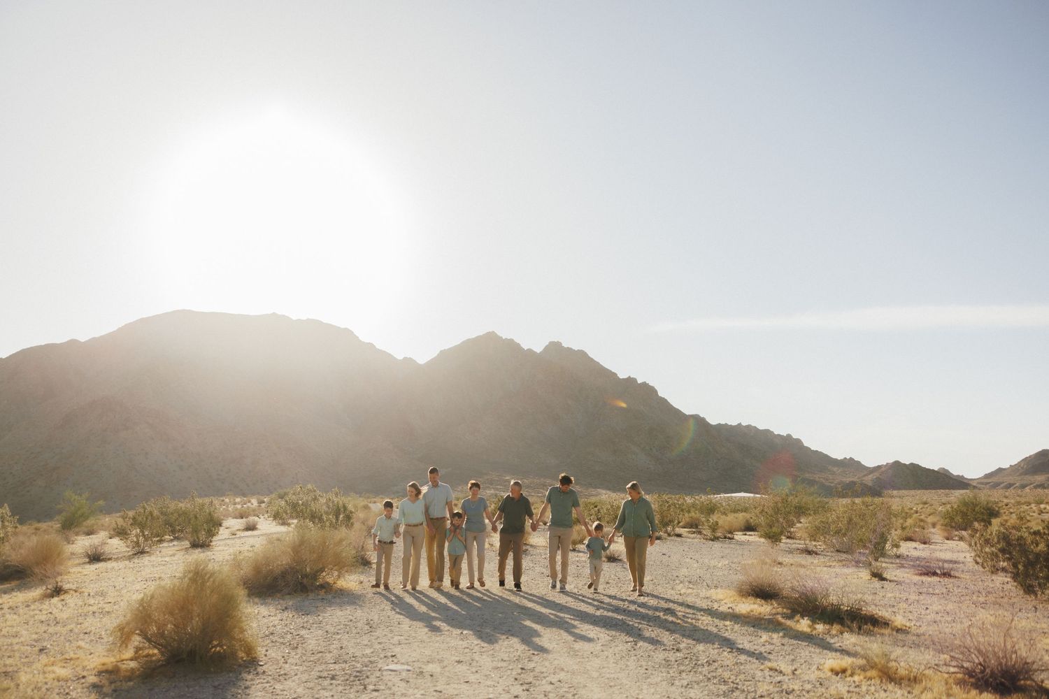 Group of friends walking together through a scenic desert landscape with mountains and bright sunlight.