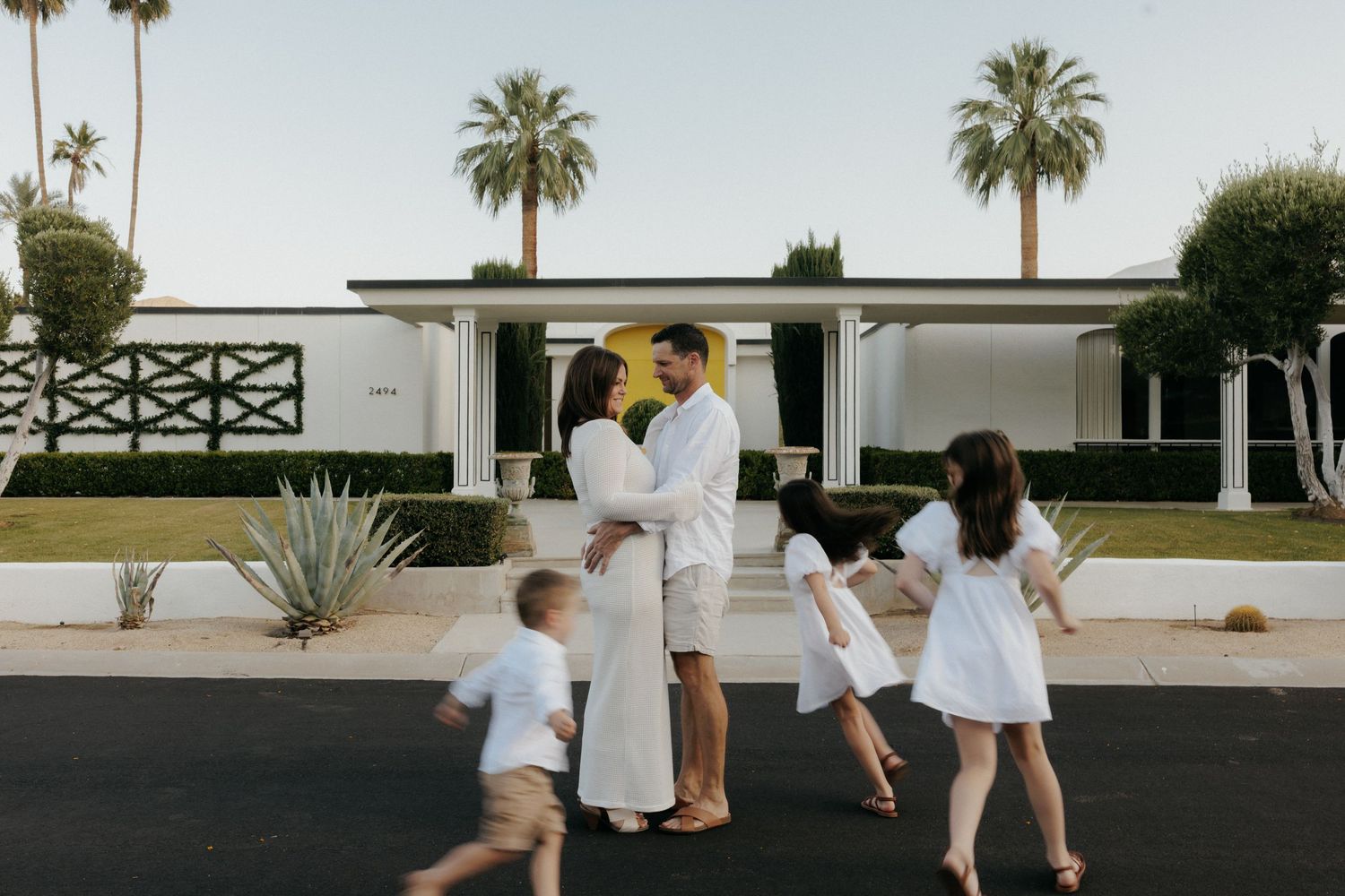 Family portrait outside a mid-century modern home in Palm Springs with palm trees and lush hedges.