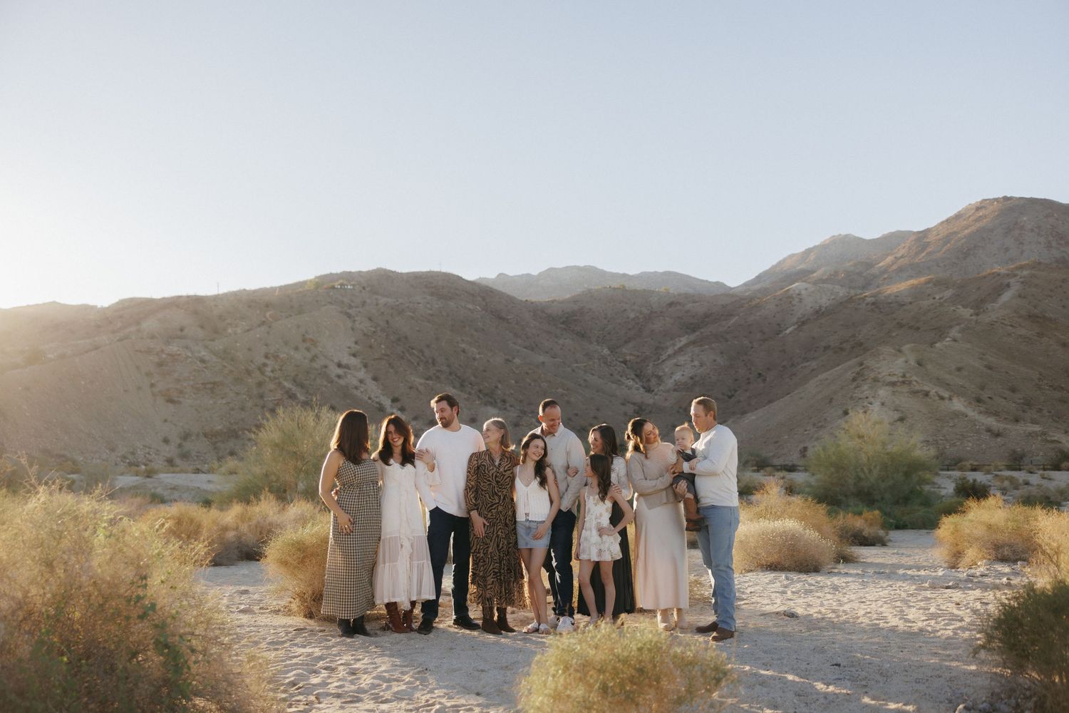 Family portrait of a large group posing in a desert landscape with golden mountains at sunset.