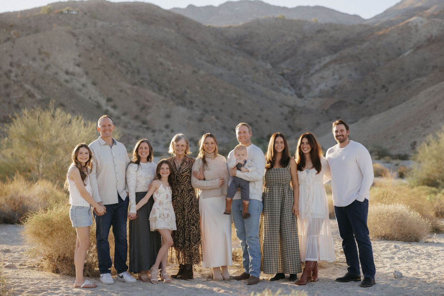 Large family group posing together outdoors in desert landscape with mountains in background during golden hour.