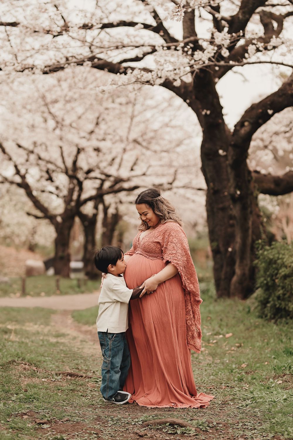 Mother and child share tender moments under pink sakura cherry blossom trees in spring garden setting.