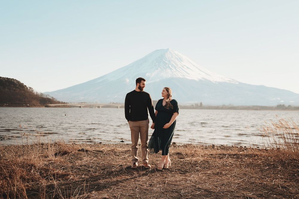 A couple stands on the shoreline gazing at Mount Fuji across the lake during golden hour in Japan.