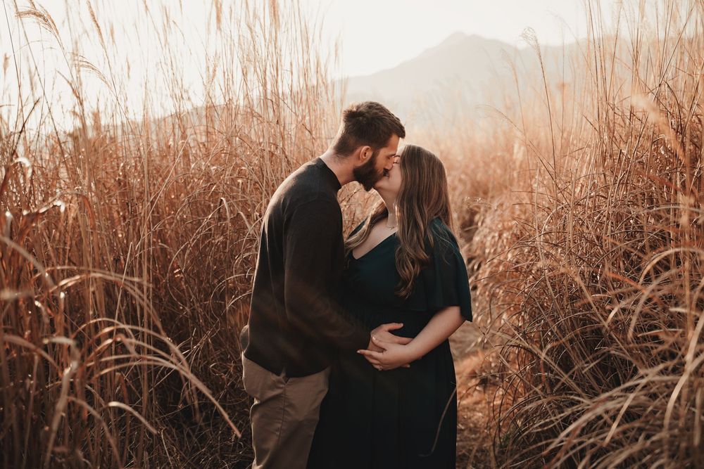 A romantic couple embraces in a golden field of tall grass during sunset, creating a silhouette against the warm sky.
