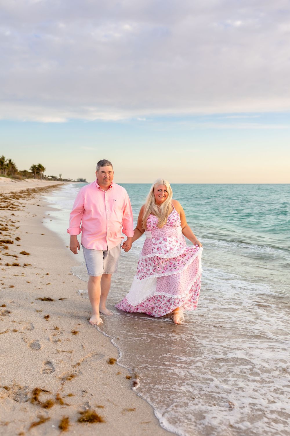 Happy couple holding hands walking along a tropical beach at golden sunset hour.