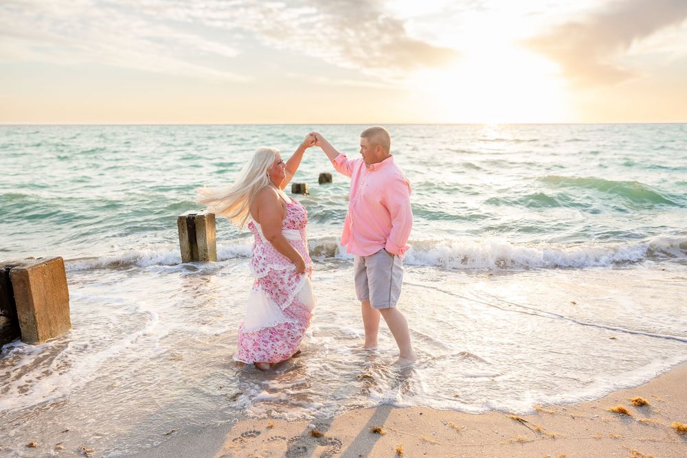 Couple dancing together on a beach at sunset, forming a heart shape with their arms.