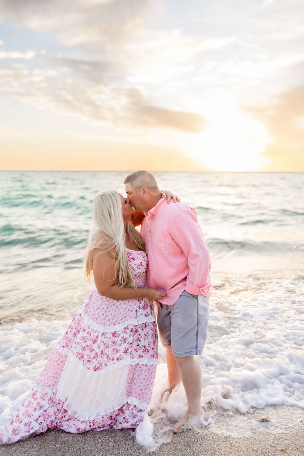 Couple sharing a romantic kiss in ocean waves at a beautiful beach sunset.