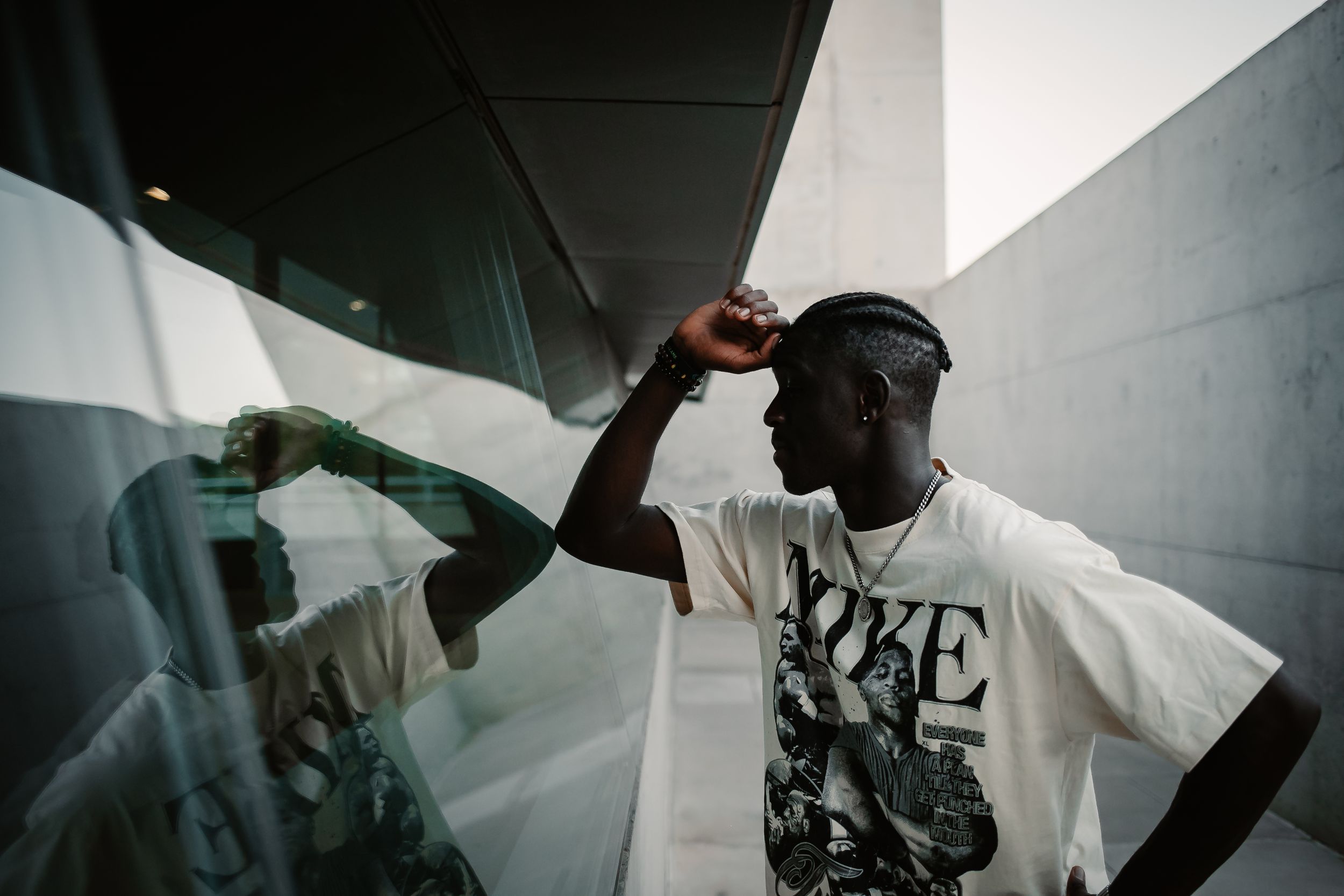 Young man in graphic tee posing near reflective glass wall in urban setting, stylish streetwear photography.