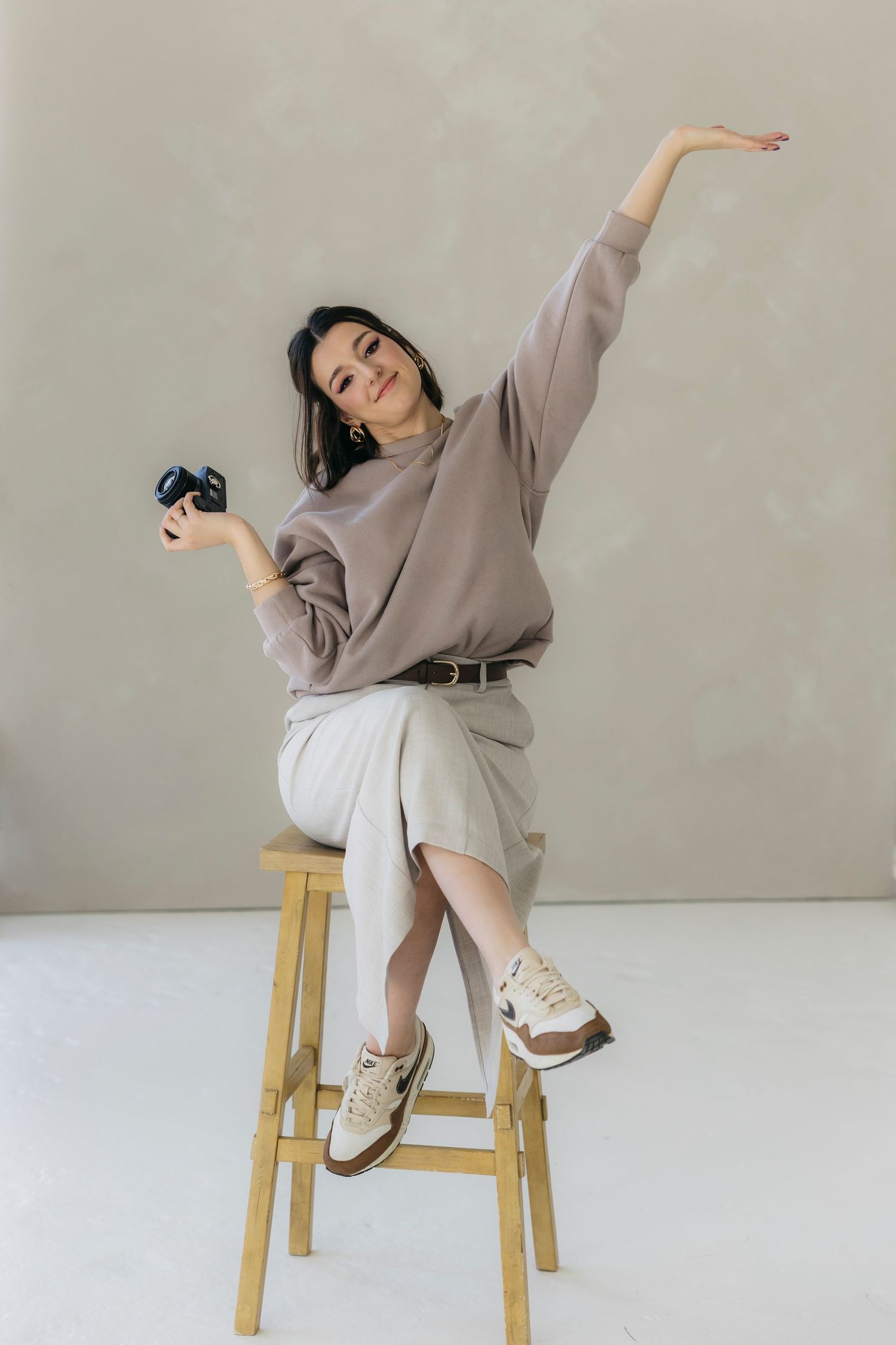 A person in casual attire strikes a dramatic pose while sitting on a wooden stool.