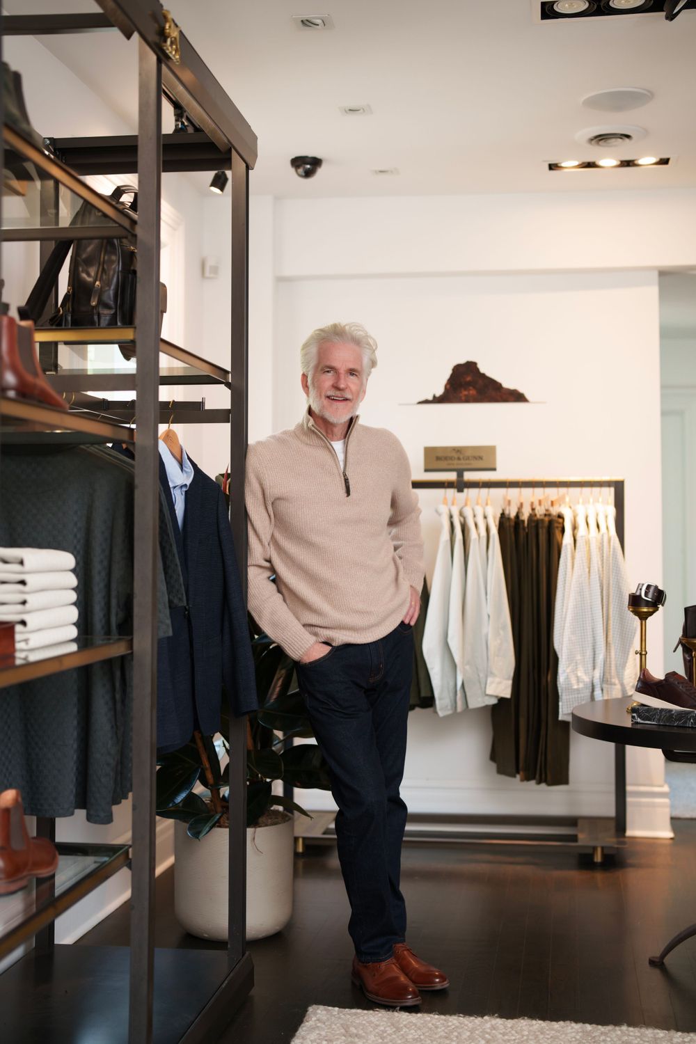 A distinguished mature man in casual attire standing in an upscale clothing boutique.