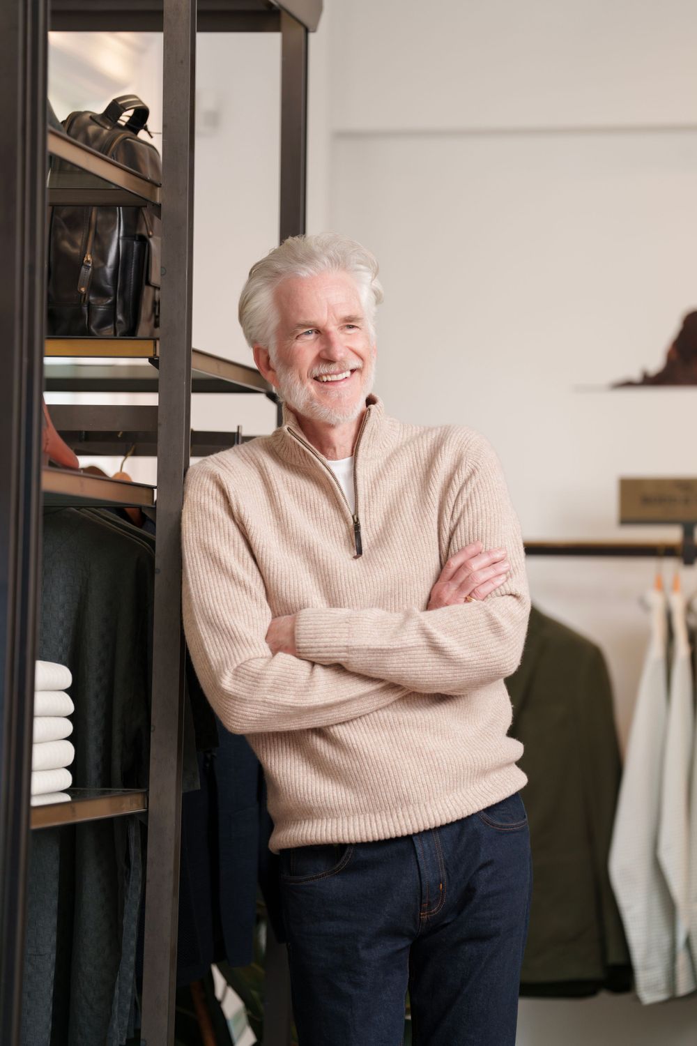 A smiling mature gentleman in a beige sweater posing in a modern retail store.