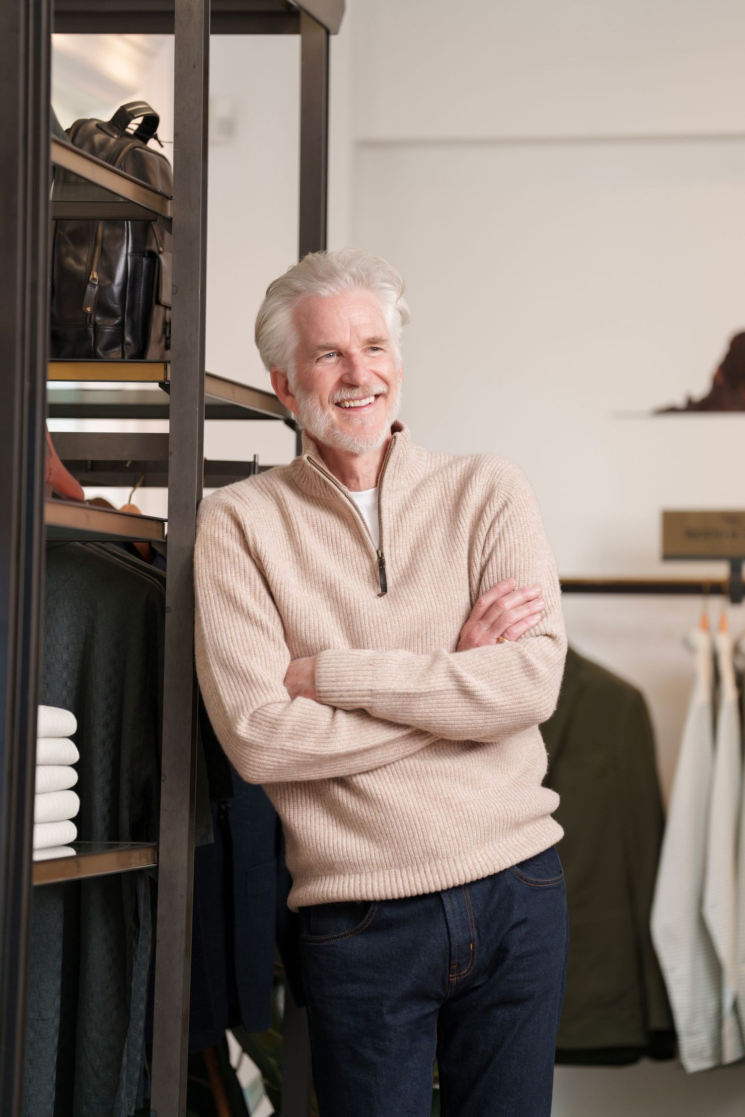 A smiling mature gentleman in a beige sweater posing in a modern retail store.