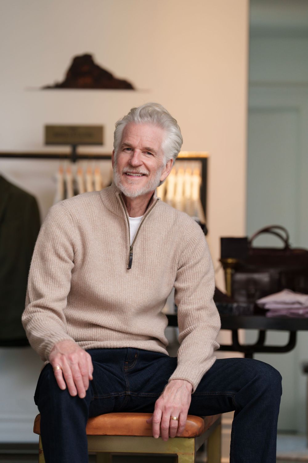 A confident senior model seated in a clothing store wearing a half-zip sweater.