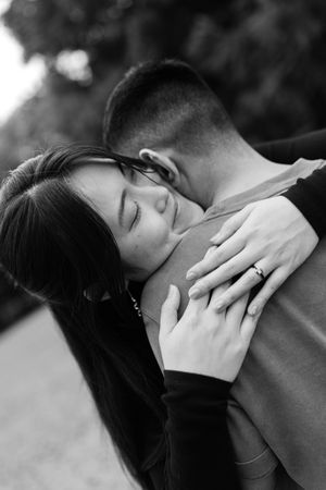 Black and white photo of a couple embracing tenderly, woman with long dark hair wearing a ring, eyes closed.